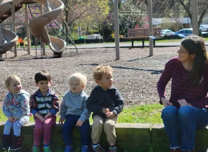 Teaching Artist Jennifer listens to feedback from participants aged 2 and 3. All sit on the edge of a neighborhood park.