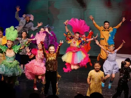 The ensemble of characters from Seussical dances the finale. The actors are in mid-air on their final jump, arms stretched wide overhead, with big smiles.